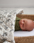 Newborn baby in a wicker crib with a white quilted blanket