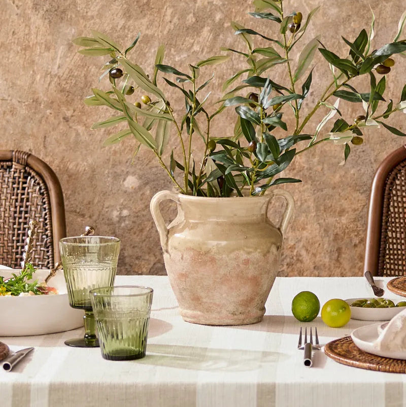 Dining table setting with a vase of greenery, glasses, and cutlery against a textured wall.