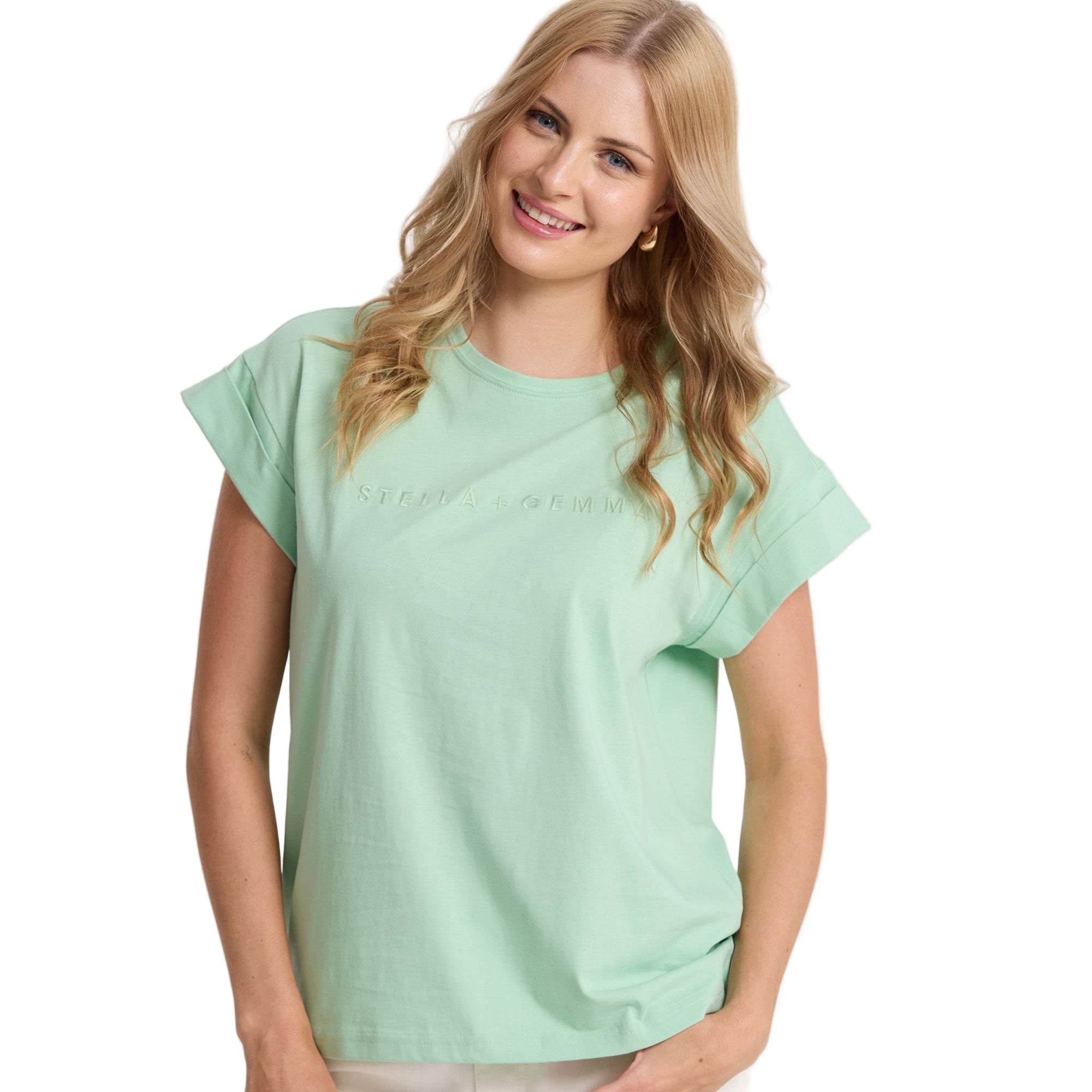 Woman wearing a light green top and white pants against a plain background