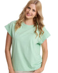Woman wearing a light green top and white pants against a plain background