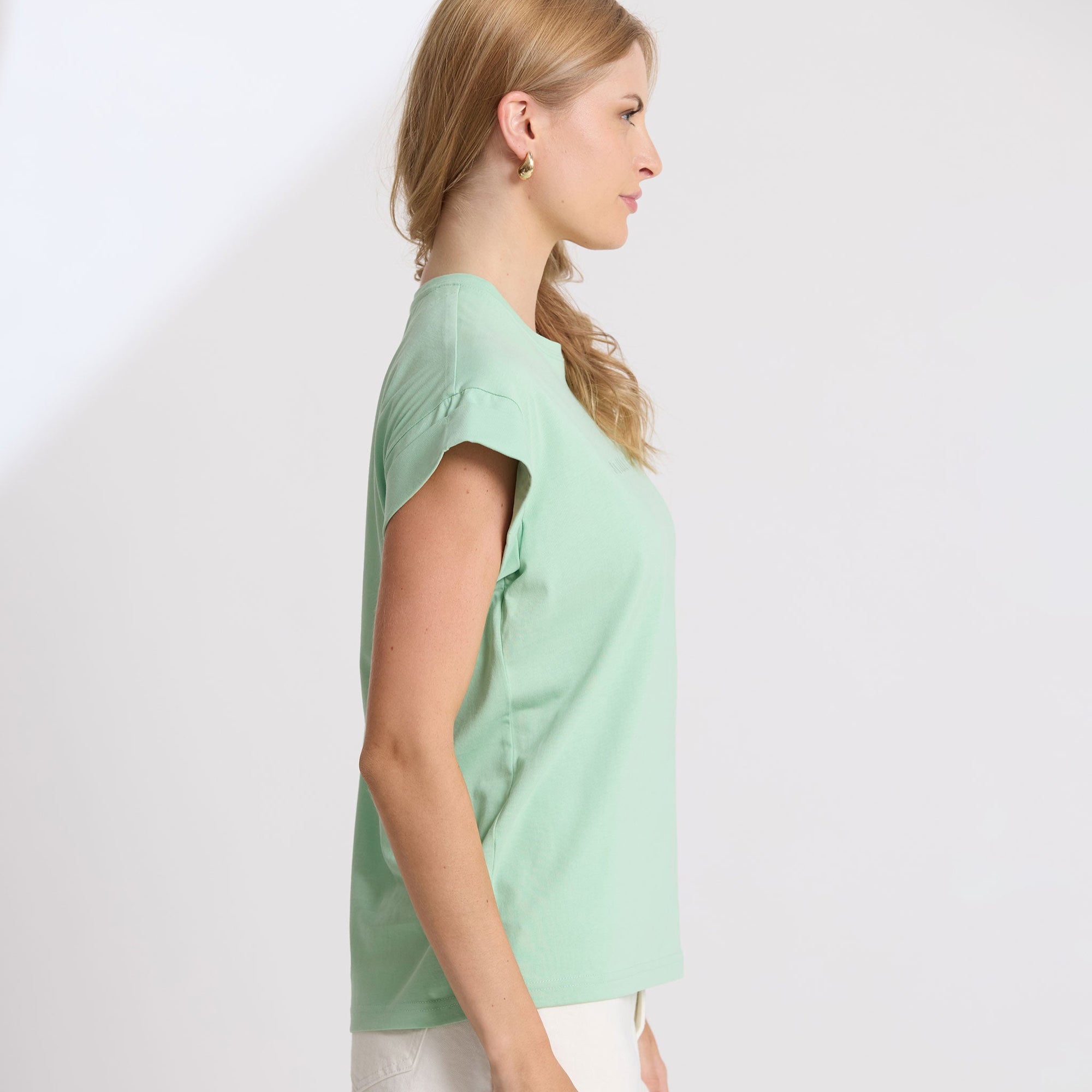 Woman wearing a light green top and white pants against a plain background