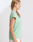 Woman wearing a light green top and white pants against a plain background