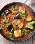 Fried eggplant and zucchini with tomato sauce in a black pan on a wooden surface