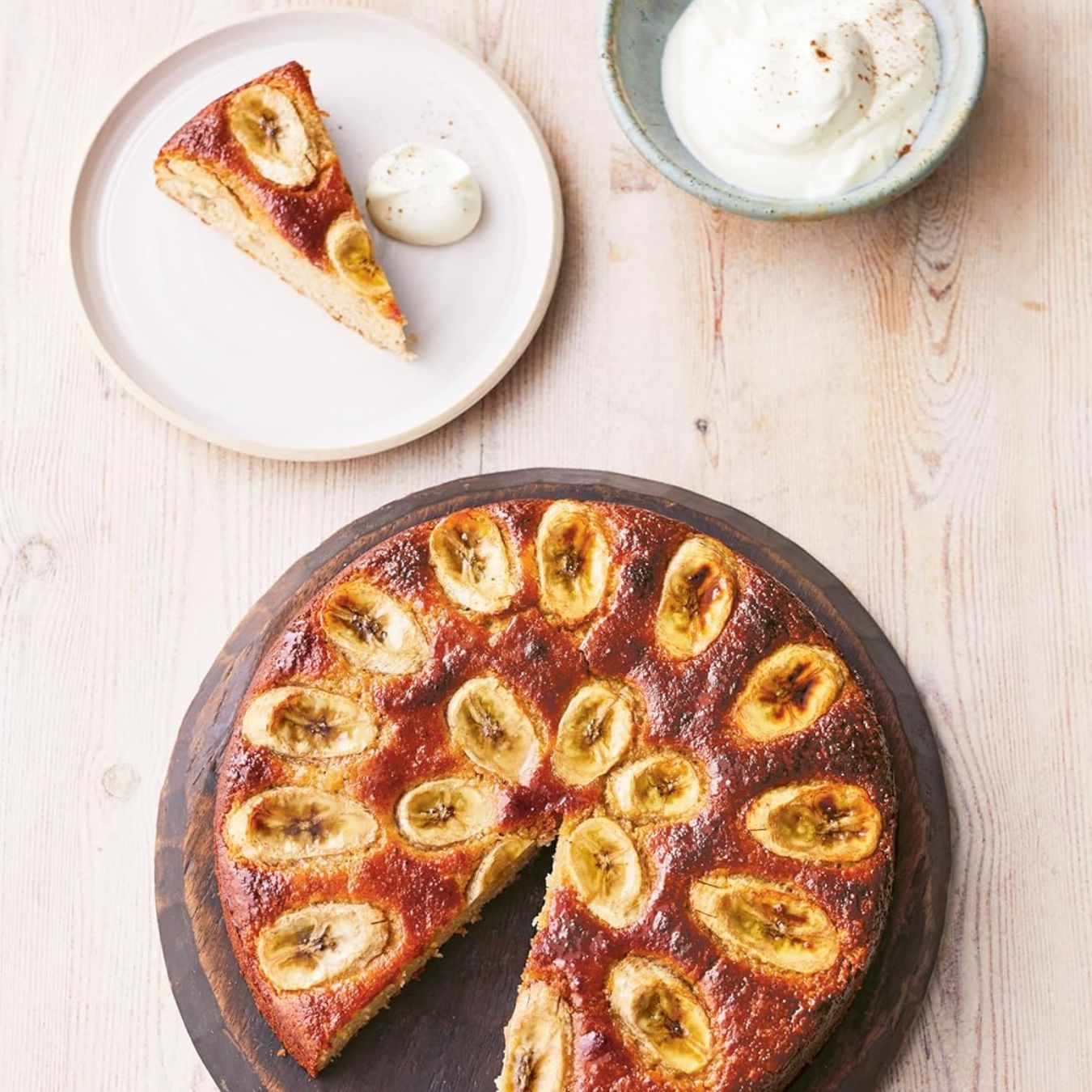 Banana cake with a slice taken out on a wooden board, served with a side of ice cream.