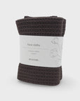 A folded pack of two dark brown knitted face cloths wrapped in a white paper band labeled 'face cloths organic cotton 2 pack ecovask' on a light gray background.