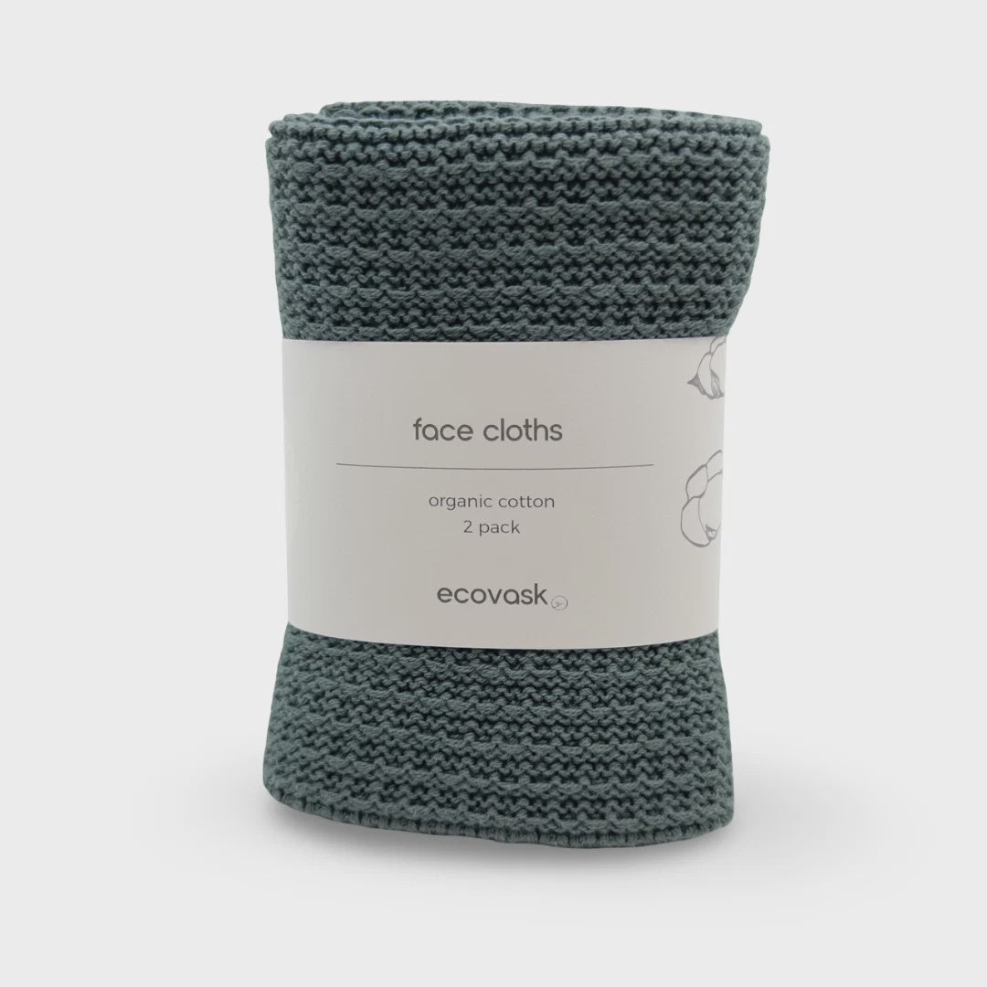 A roll of knitted face cloths in a muted teal-green color, wrapped with a white paper label that reads 'face cloths', 'organic cotton', '2 pack', and the brand name 'ecovask'.
