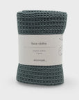 A roll of knitted face cloths in a muted teal-green color, wrapped with a white paper label that reads 'face cloths', 'organic cotton', '2 pack', and the brand name 'ecovask'.