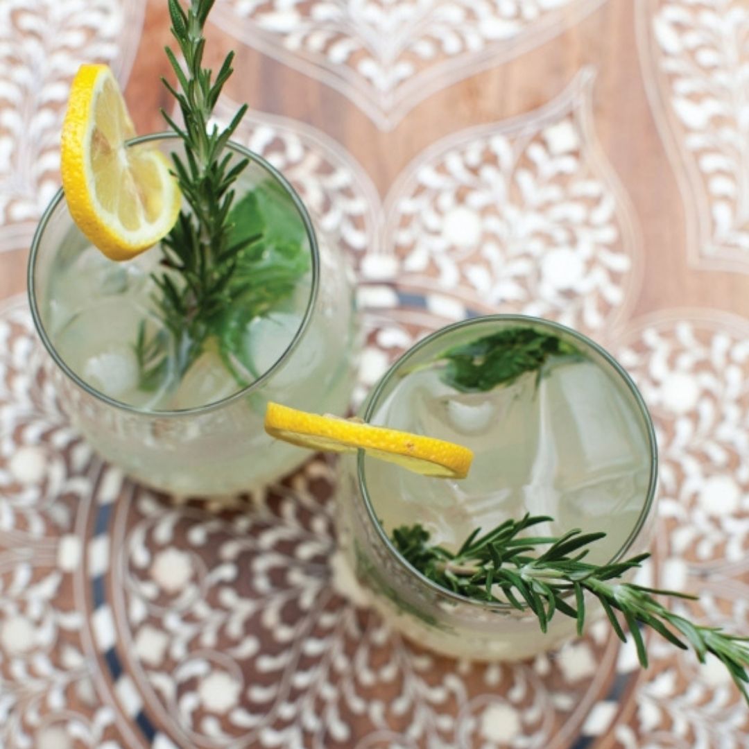 Two glasses of cocktails with lemon slices and rosemary on a patterned surface