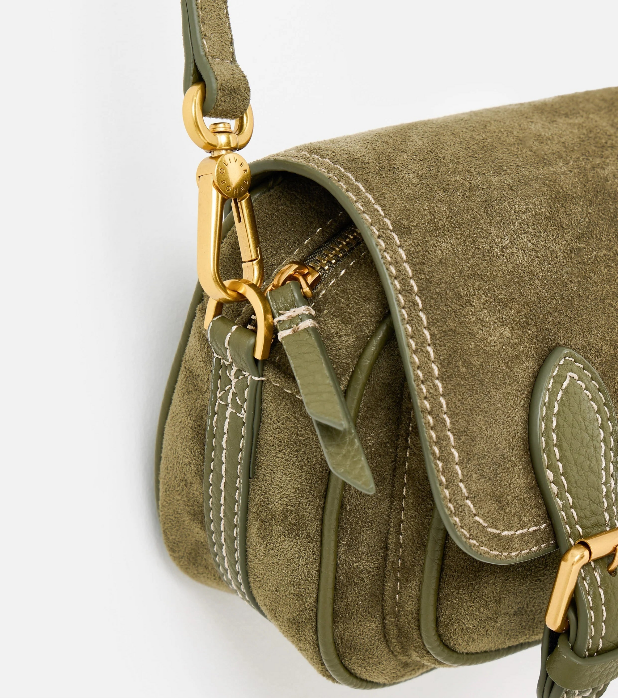 Close-up of an olive green suede crossbody bag with gold-tone hardware, white contrast stitching, and a matching green leather strap on a white background.