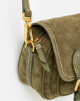 Close-up of an olive green suede crossbody bag with gold-tone hardware, white contrast stitching, and a matching green leather strap on a white background.