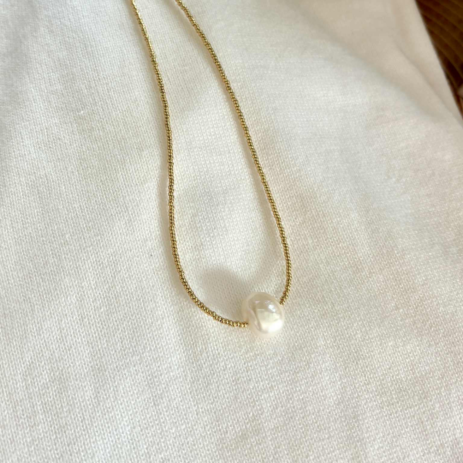 Gold necklace with a single pearl pendant on a white fabric background