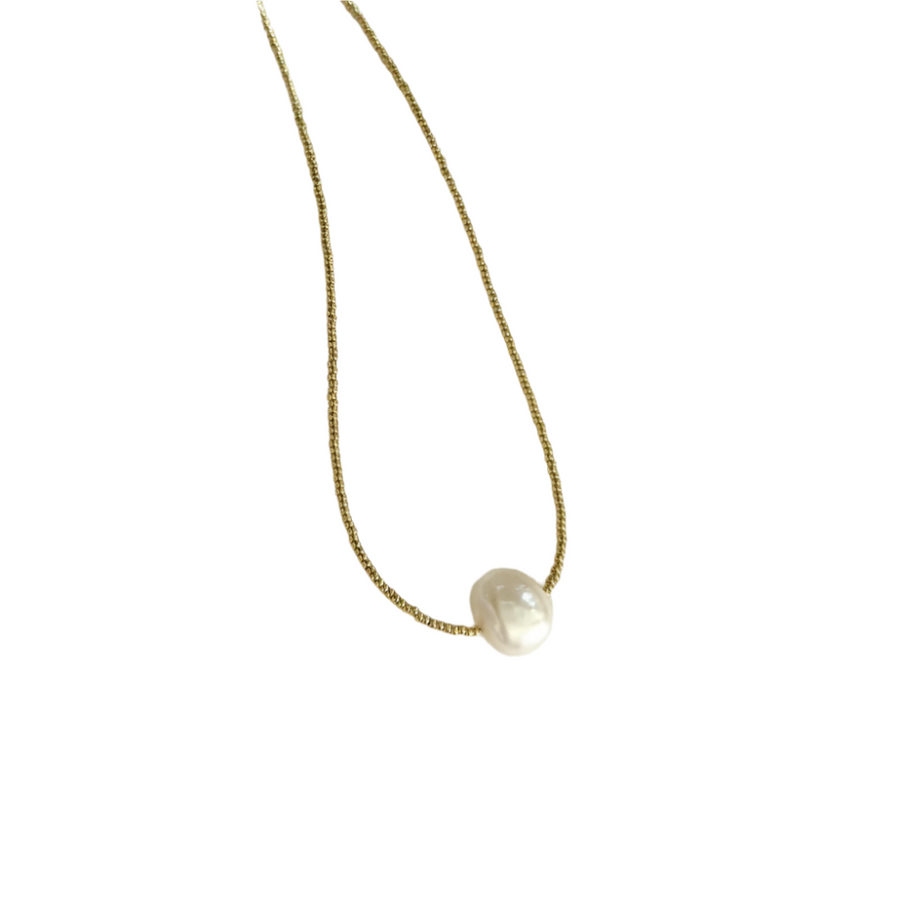 Gold necklace with a single pearl pendant on a white fabric background