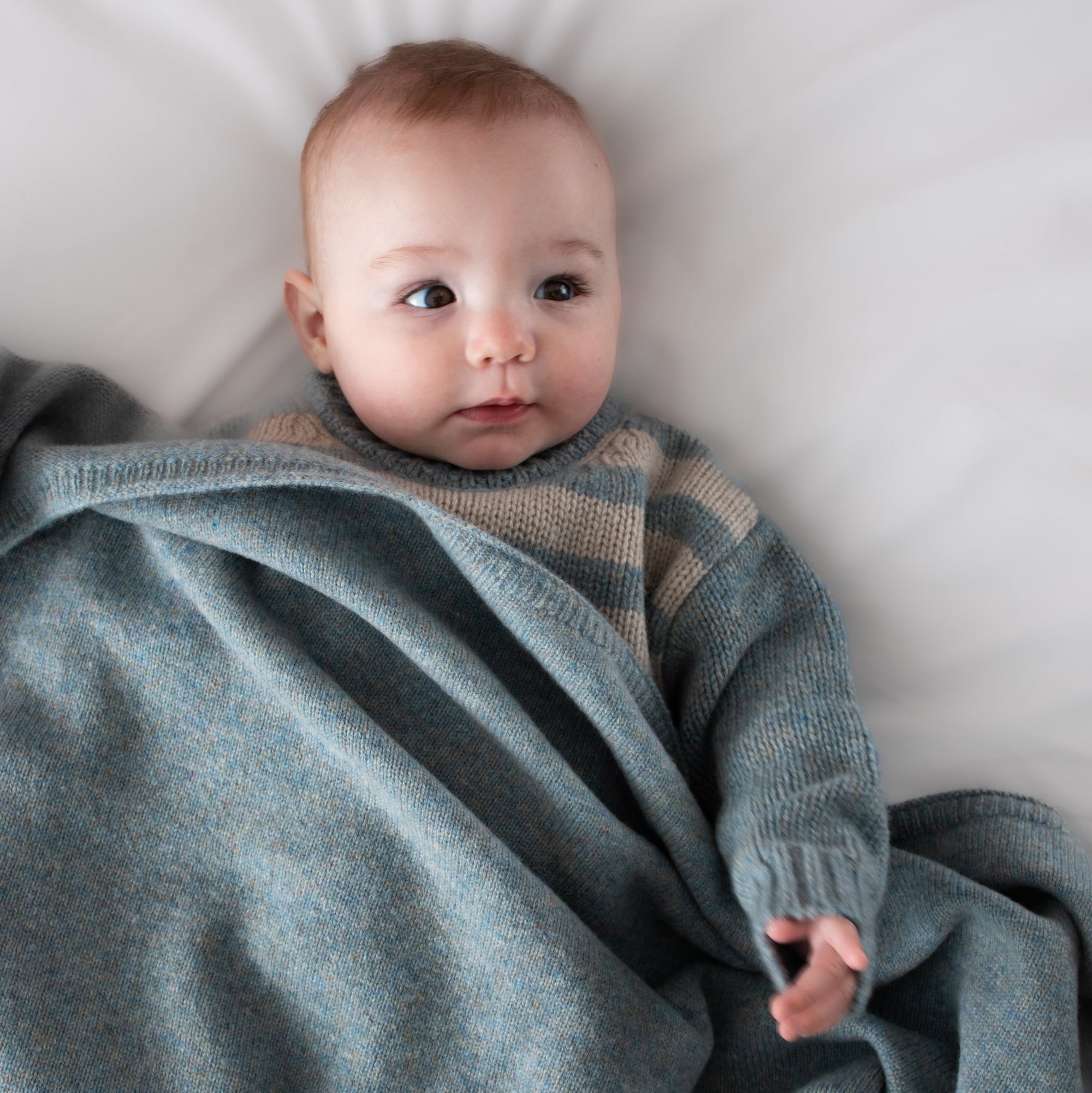 Baby wrapped in a gray blanket on a white surface