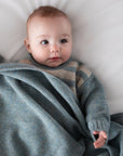 Baby wrapped in a gray blanket on a white surface
