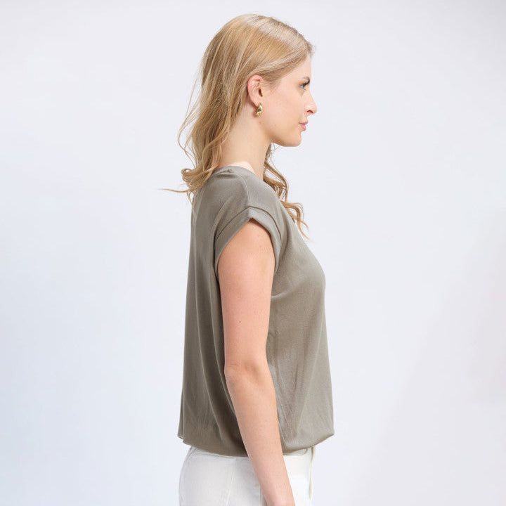 Woman wearing a green sleeveless top and white pants on a light gray background