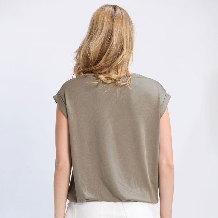 Person wearing a green sleeveless top and white pants on a light gray background