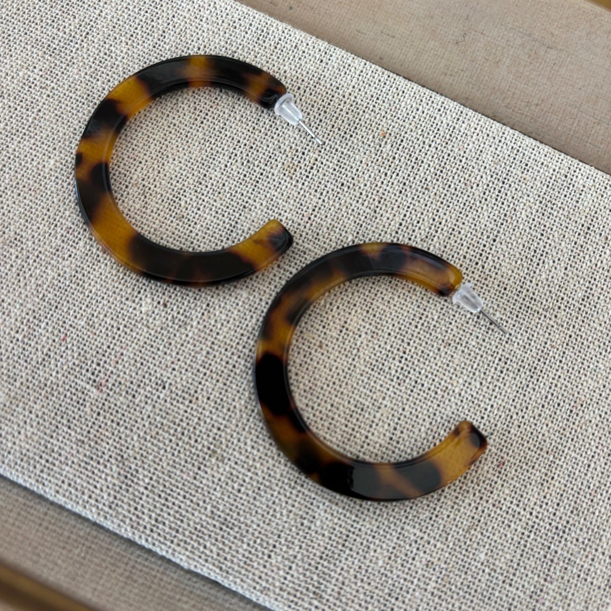 Tortoiseshell hoop earrings on a textured fabric surface