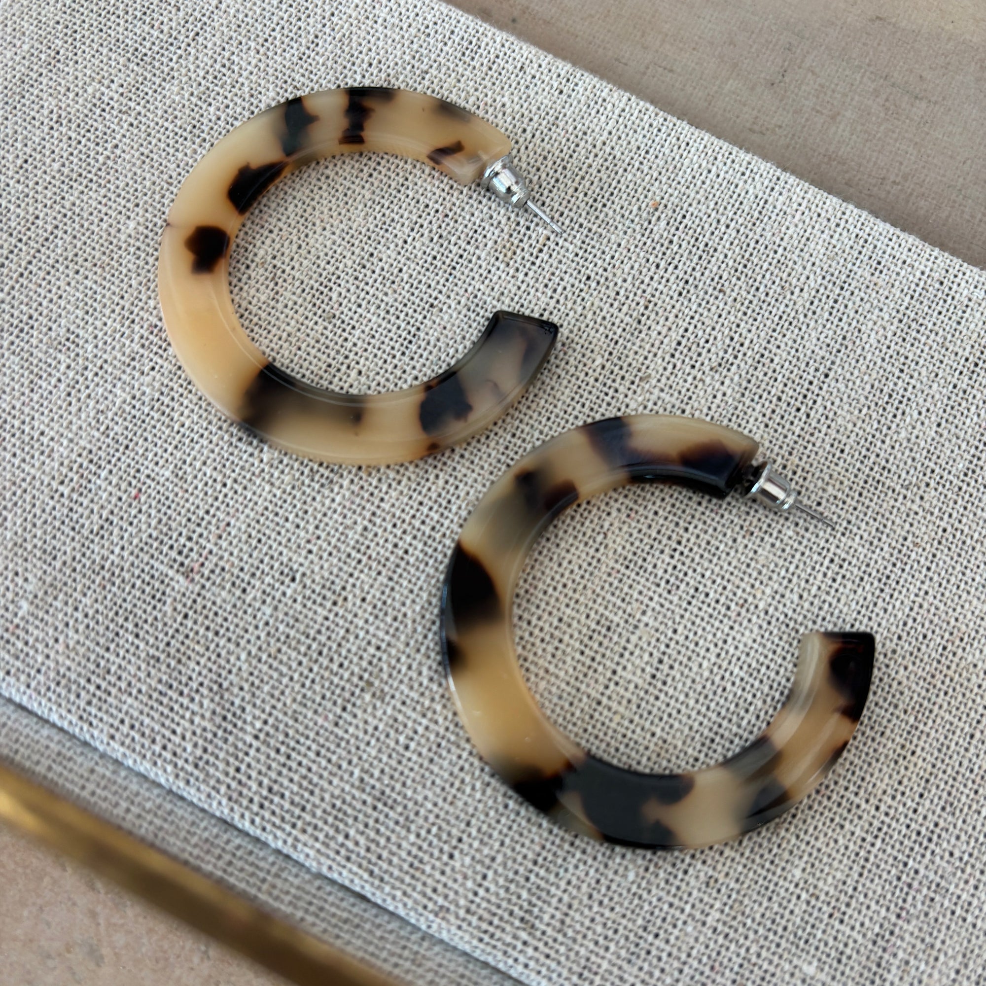 Pair of tortoiseshell hoop earrings on a textured surface
