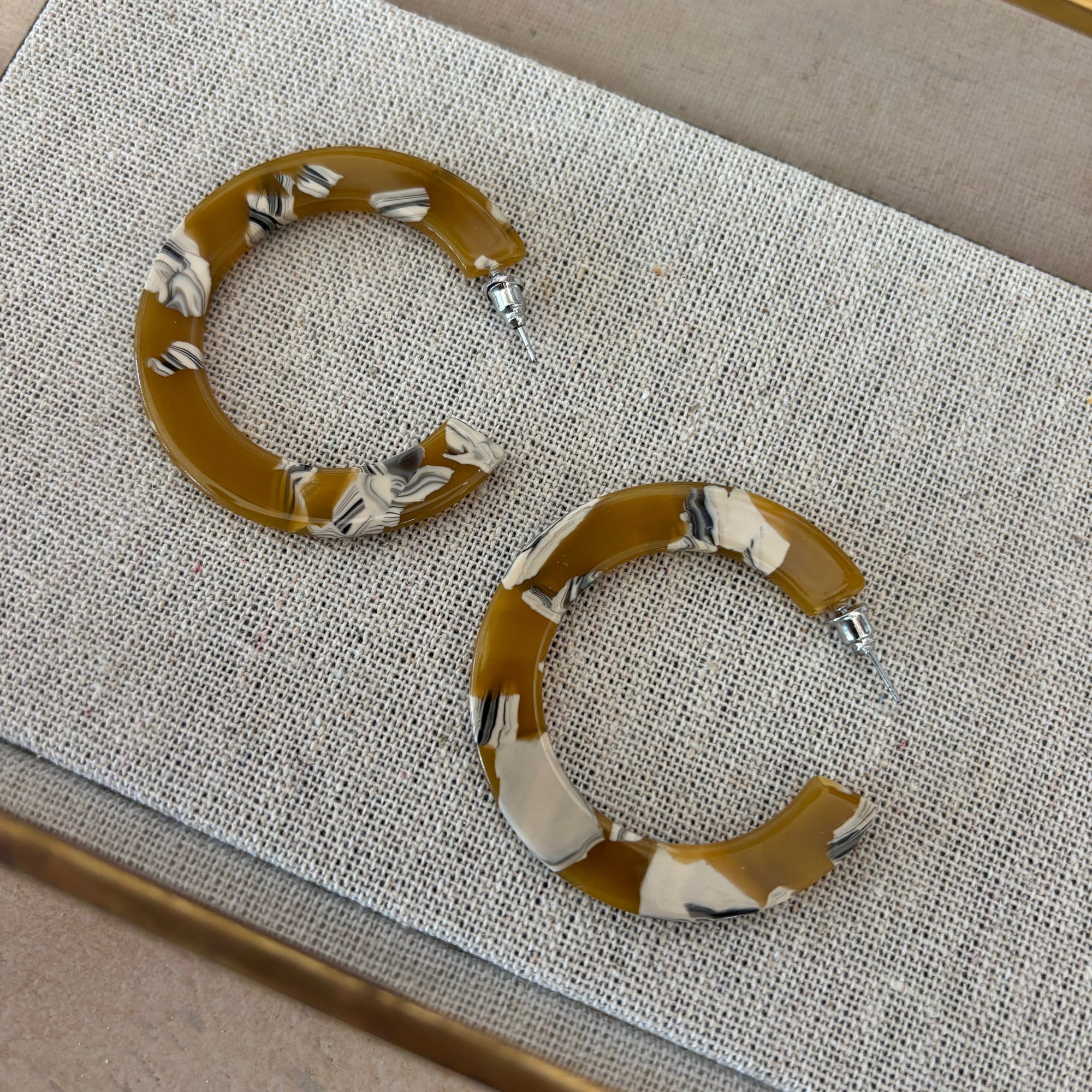 Pair of brown hoop earrings with decorative patterns on a textured surface