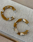 Pair of brown hoop earrings with decorative patterns on a textured surface